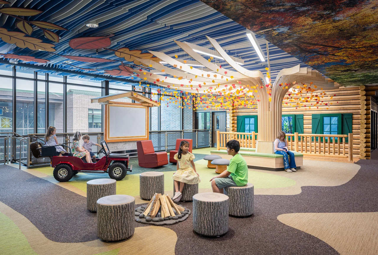 Students sit among tree-shaped tables beneath a colorful canopy.