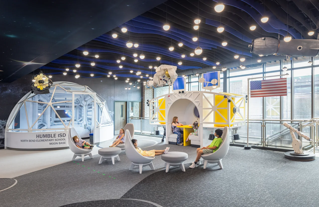 Space-themed learning area with a capsule, telescope and illuminated planets beneath a dark ceiling.
