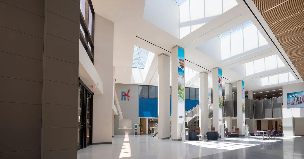 Sunlight fills the renovated conference-center atrium, with tall digital display columns, a stair, and seating beneath skylights.